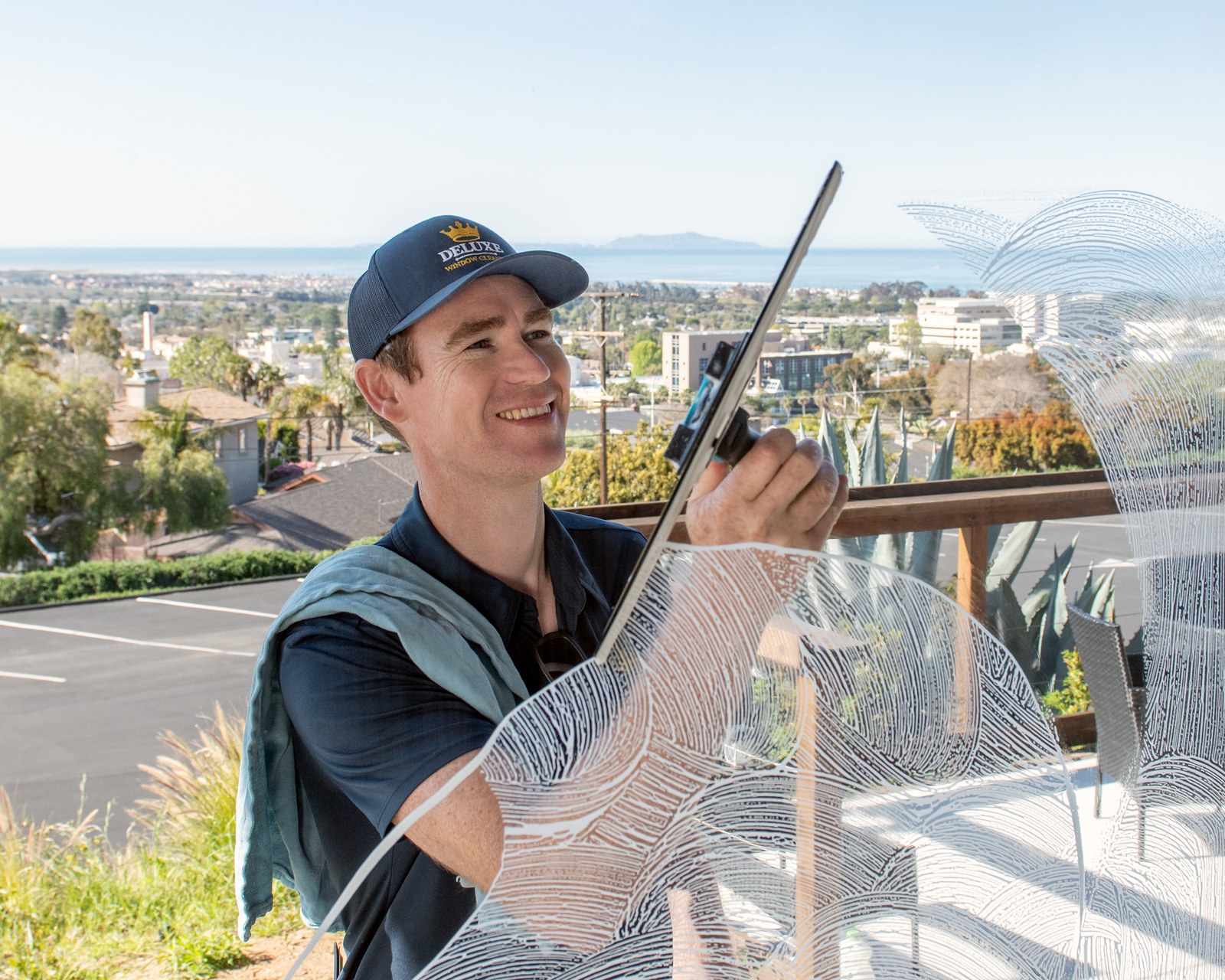 Deluxe Window Cleaning owner squeegeeing a window above Ventura